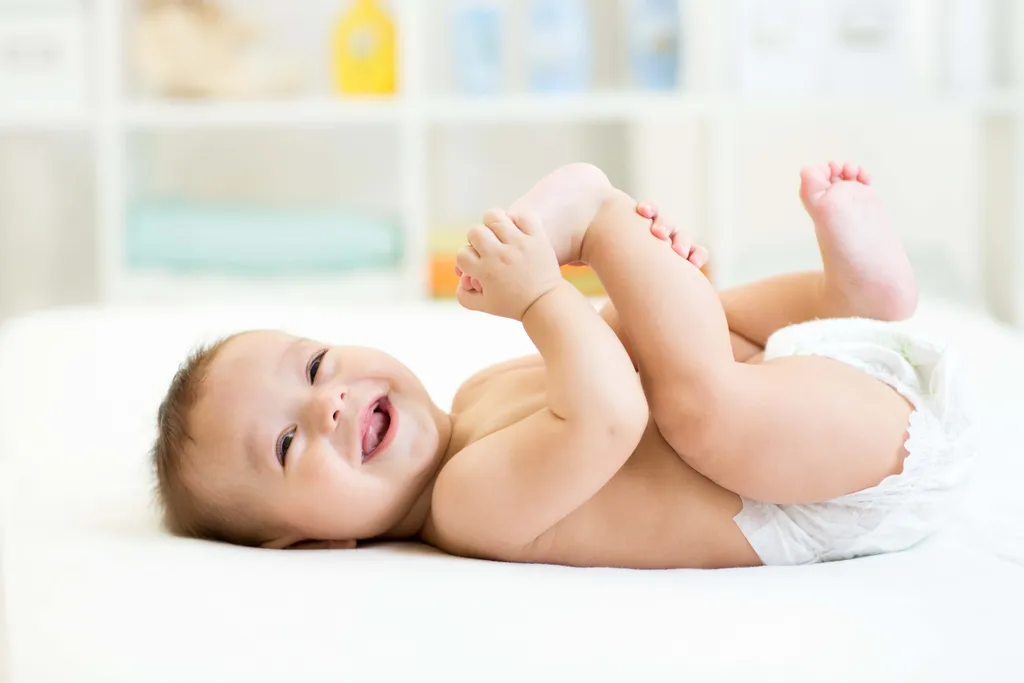 Lachendes Baby liegt mit Windel auf einer weichen Unterlage