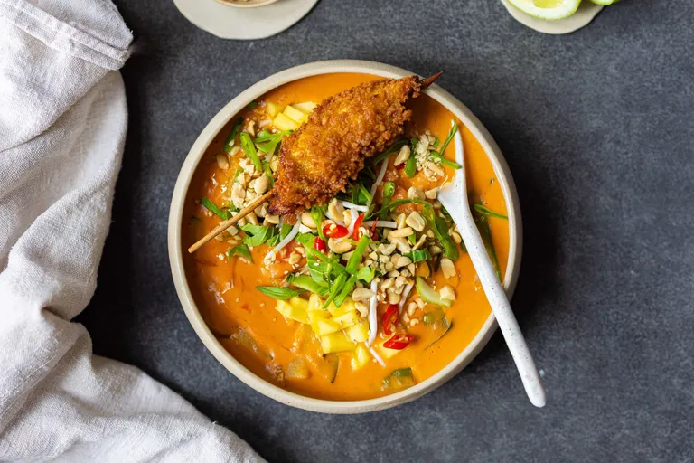 Cremige Thai-Kokos-Curry-Suppe mit Gemüse, Mango, Erdnüssen und knusprigem Hähnchenspieß