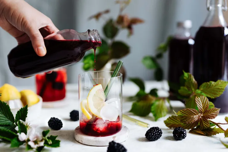 Brombeersirup wird in ein Glas mit Eiswürfeln und Zitronenscheiben für eine erfrischende Limonade gegossen