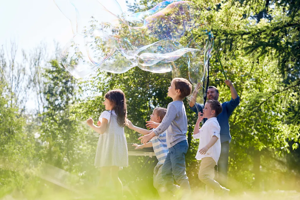 Eine Gruppe Kinder mit einem Vater spielen mit Riesen-Seifenblasen