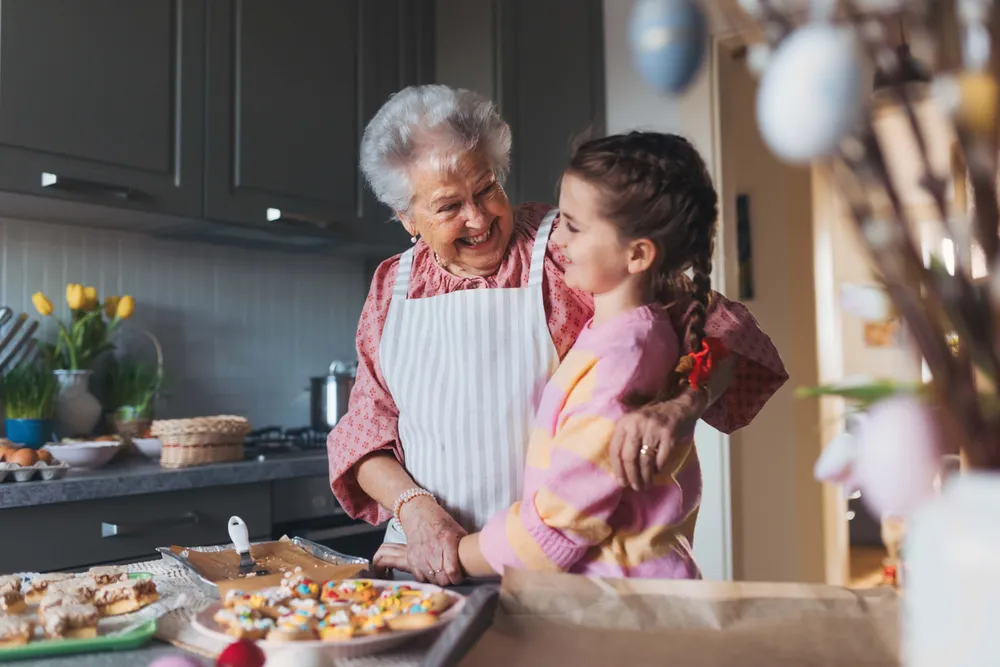 Großmutter und Enkelin genießen es, gemeinsam in einer gemütlichen Küche zu backen, umgeben von Plätzchen und bunten Dekorationen.