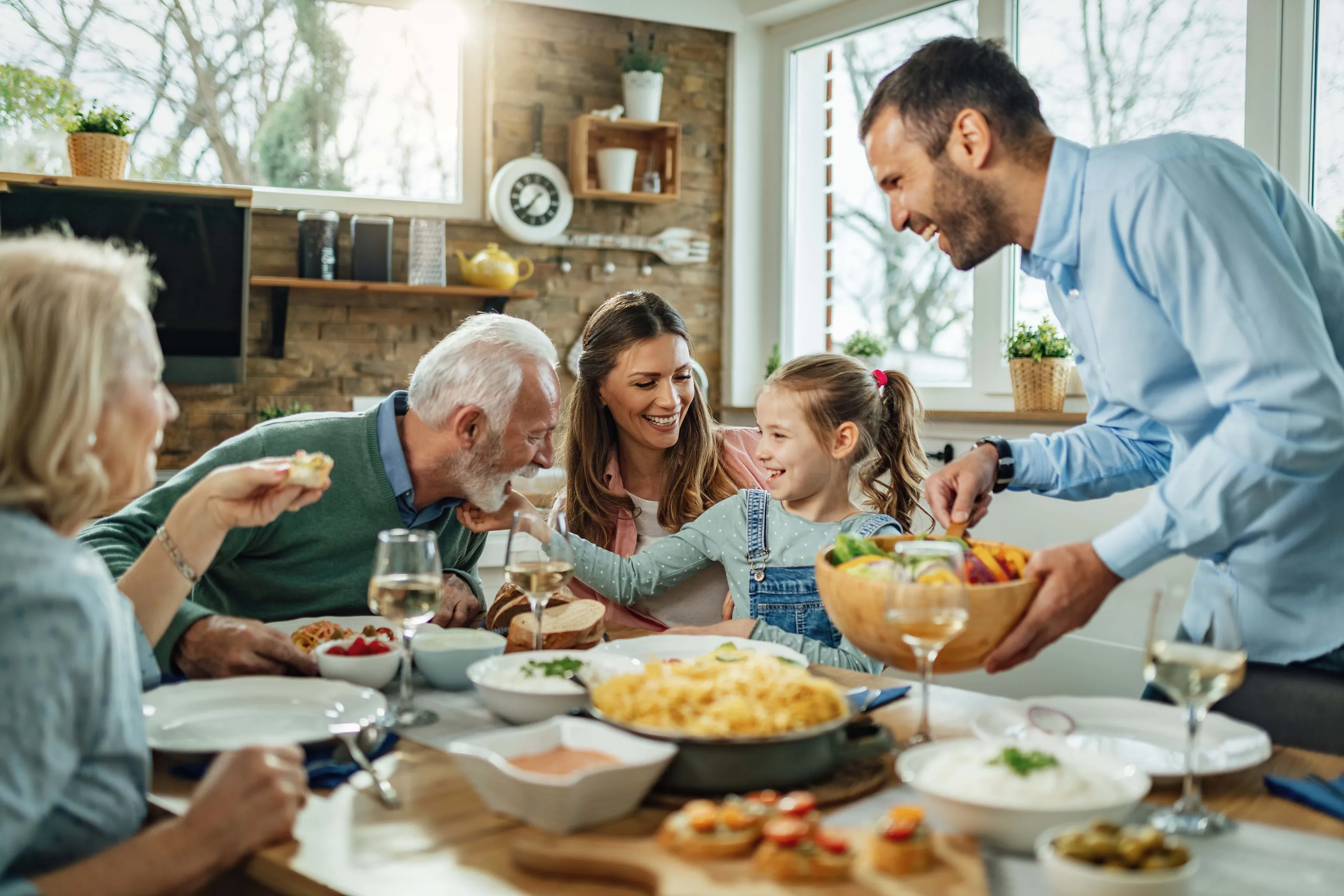 Eine Familie genießt gemeinsam ein fröhliches Essen an einem Tisch mit verschiedenen Gerichten und teilt Lachen und Geselligkeit in einem hellen Esszimmer.
