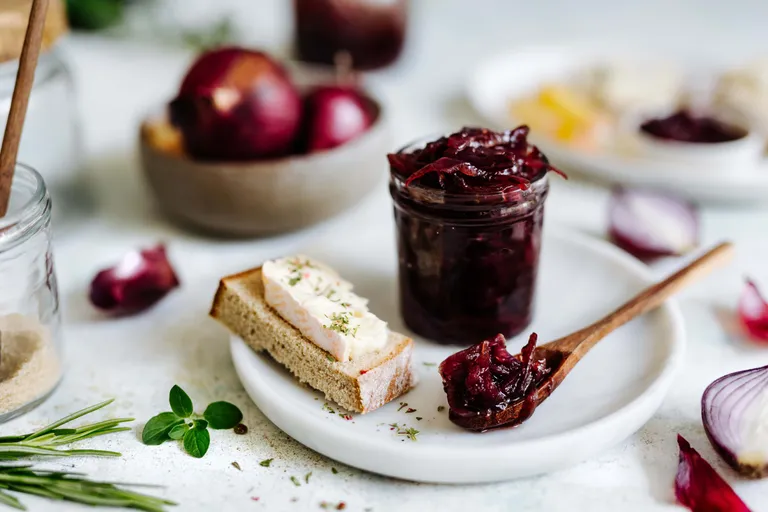 Selbstgemachte rote Zwiebel-Marmelade im Glas mit Gewürzen und Holzlöffel