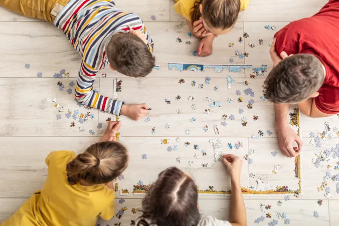 Familie liegt mit dem Kopf zusammen am Boden, Puzzlestücke sind verteilt neben ihnen