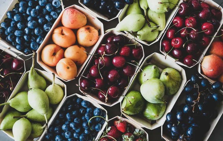 Eine Auswahl an Obst in Körben, darunter Heidelbeeren, Aprikosen, Kirschen, Birnen, Erdbeeren und Feigen, präsentiert auf einem dunklen Untergrund.