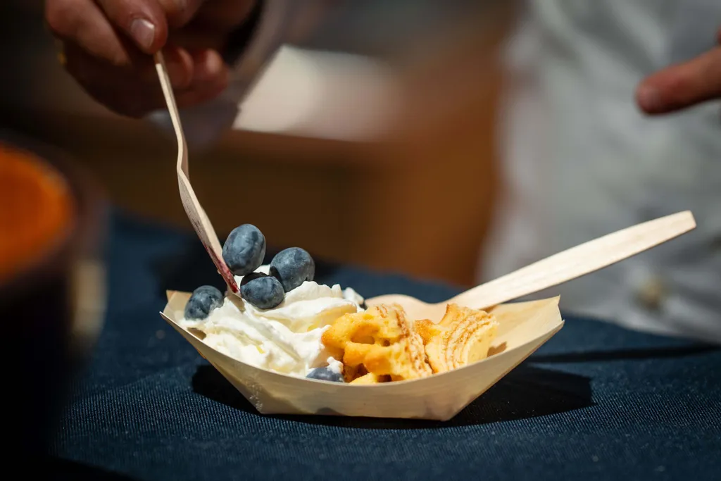 Eine Person beim Probieren einer Verkostschale mit Schlagobers, Heidelbeeren und Waffeln