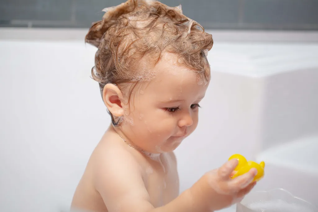Kleinkind spielt beim Baden mit einer gelben Quietscheente