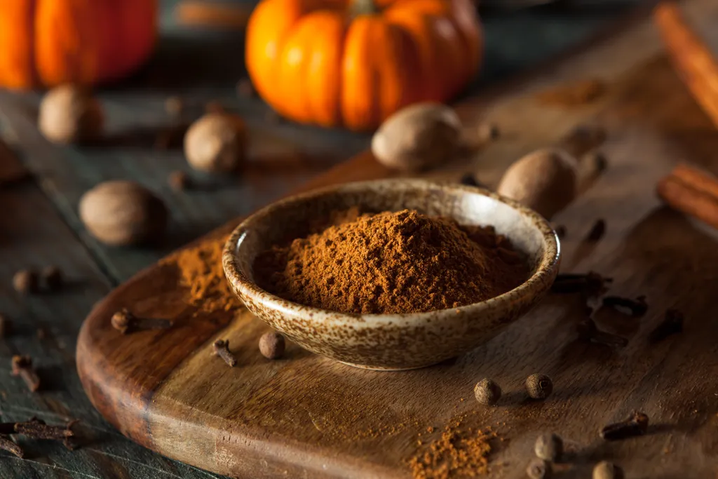 Ein Schälchen mit Pumpkin Spice auf einem Holzbrett vor dunklem HIntergrund mit Kürbissen