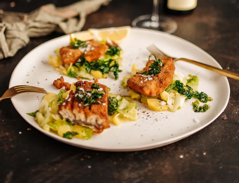Ein gebackener Karpfen mit Kartoffelsalat und grünem Gemüse auf einem weißen Teller angerichtet