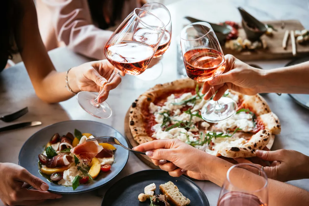 Freunde genießen Pizza, Antipasti und Roséwein bei einem gemeinsamen italienischen Abendessen