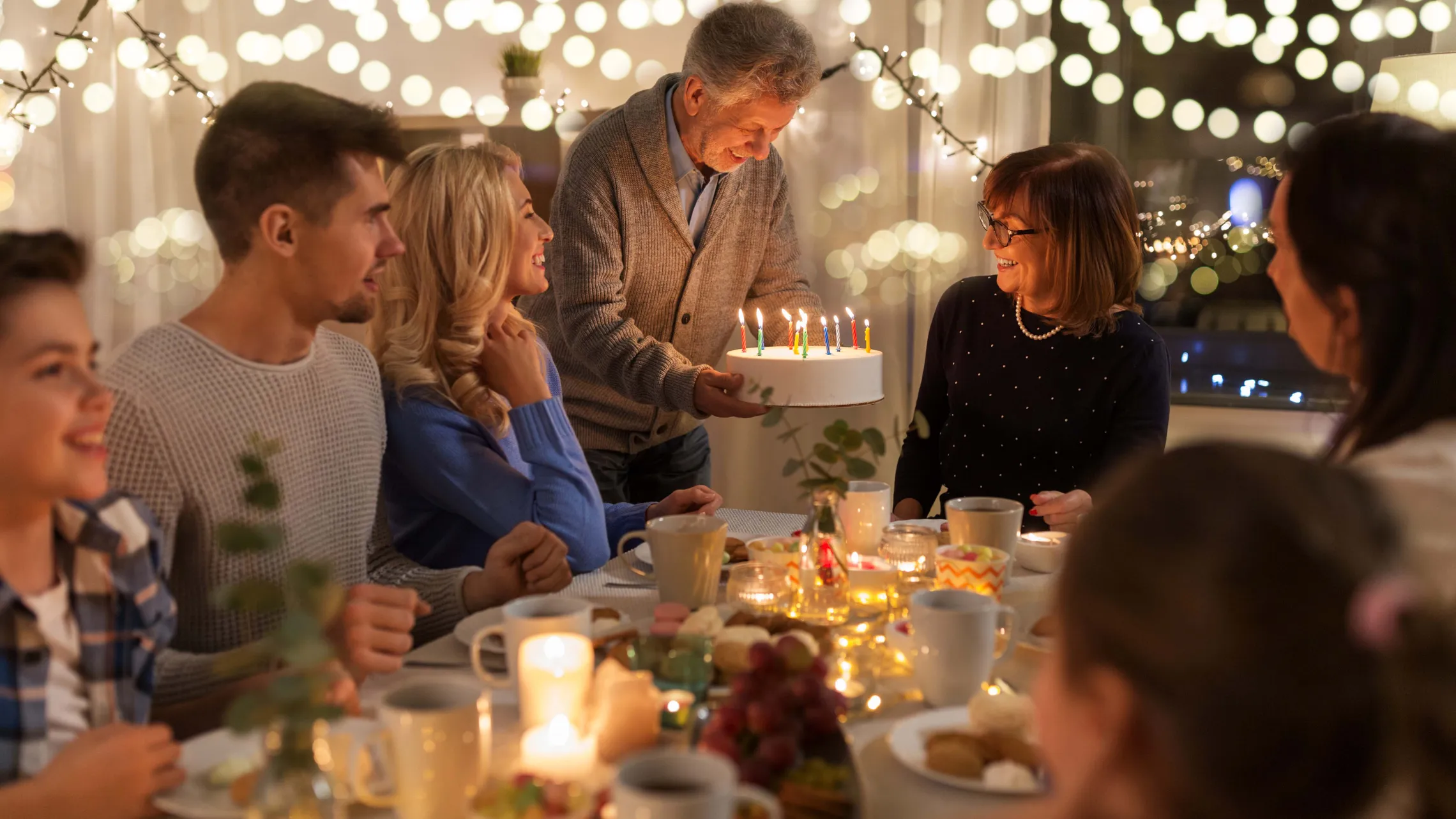 Familie feiert gemeinsam einen Geburtstag mit beleuchteter Geburtstagstorte und Kerzen