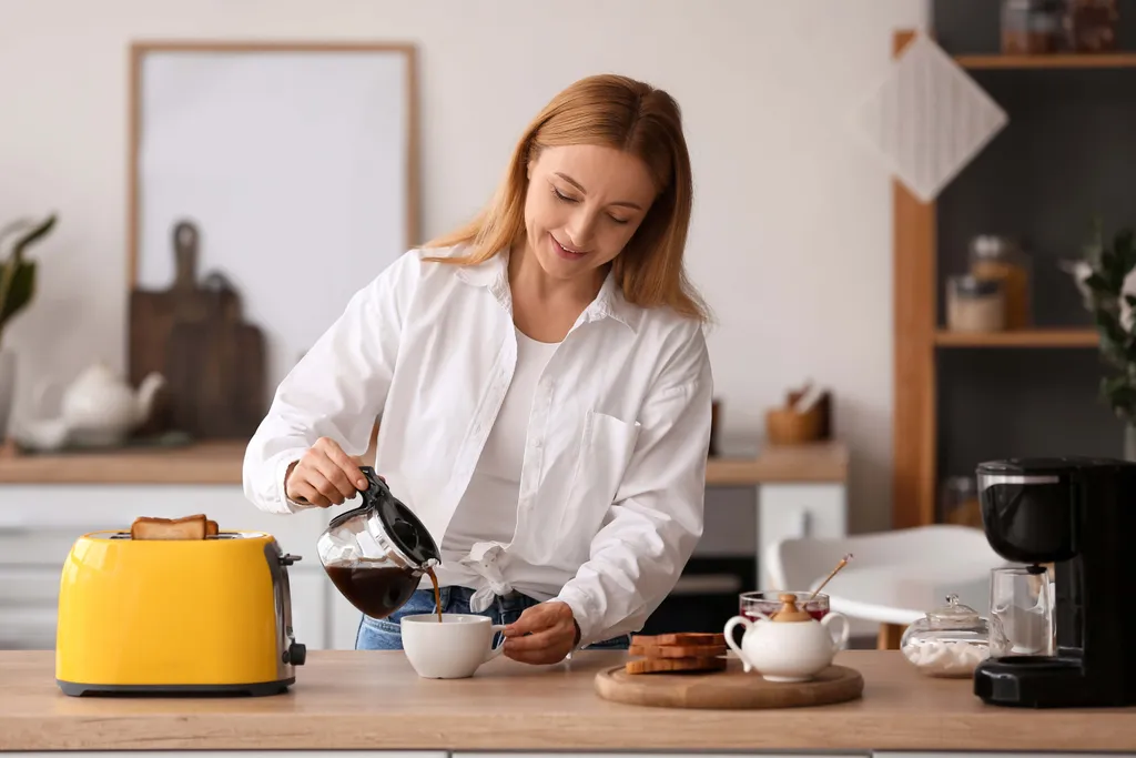 Eine Frau in einer Küche, die Kaffee in eine Tasse gießt; daneben stehen ein gelber Toaster und ein Teller mit Toast.