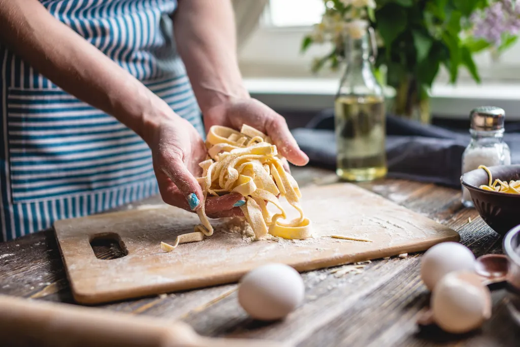 Eine Person macht Pasta selbst, hält Nudeln in den Händen in einer Küche mit Schneidebrettern und Zutaten