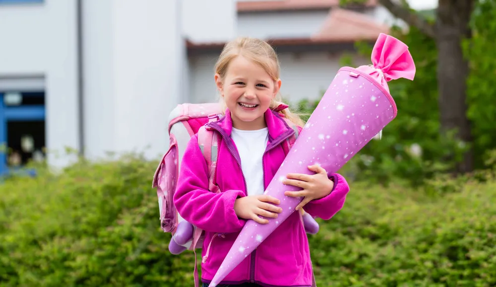 Fröhliches Mädchen mit Schultüte und Schulrucksack am ersten Schultag