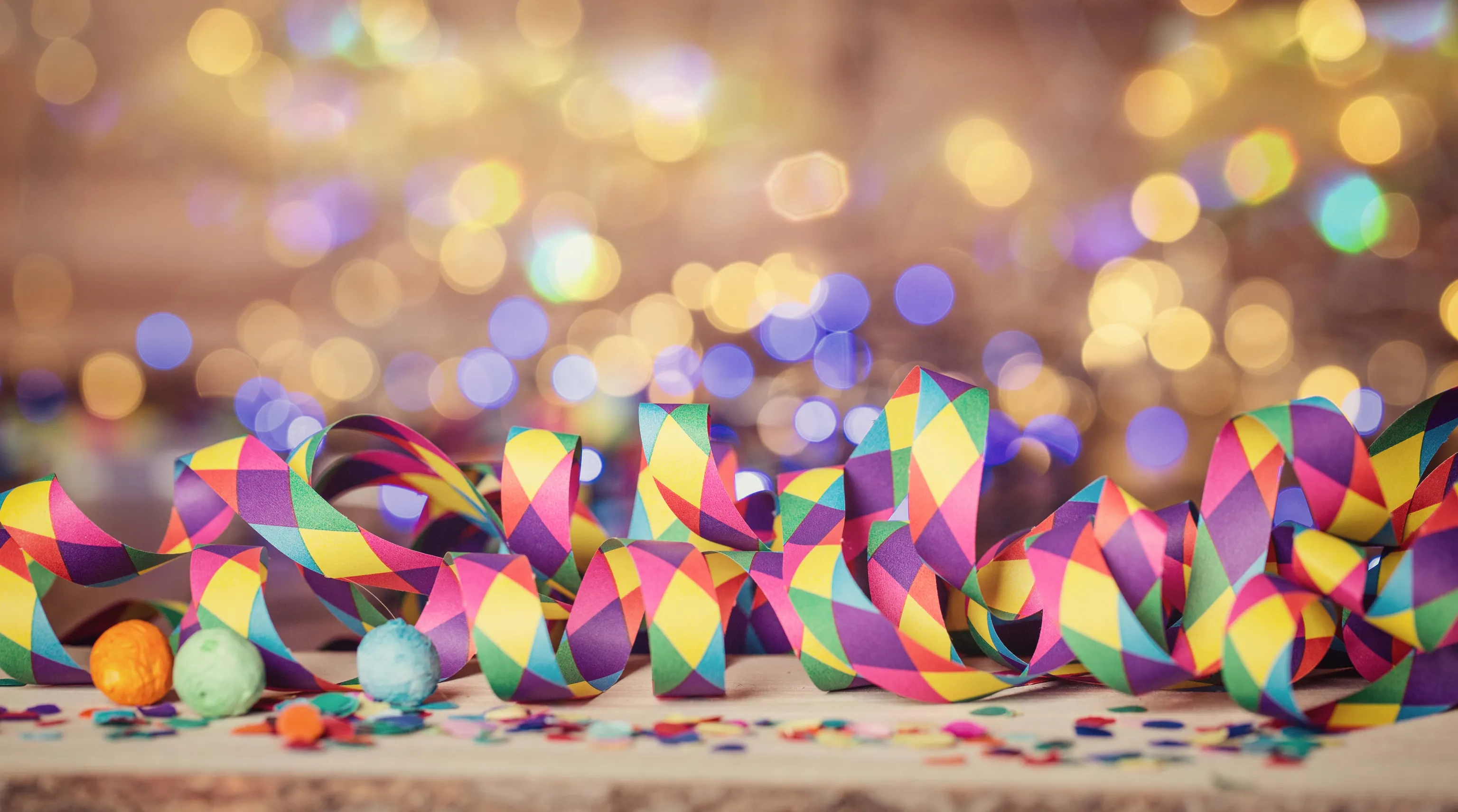 Bunte Papierschlangen und Konfetti vor einem Bokeh-Hintergrund aus warmen und kühlen Lichtern sorgen für eine festliche Atmosphäre.