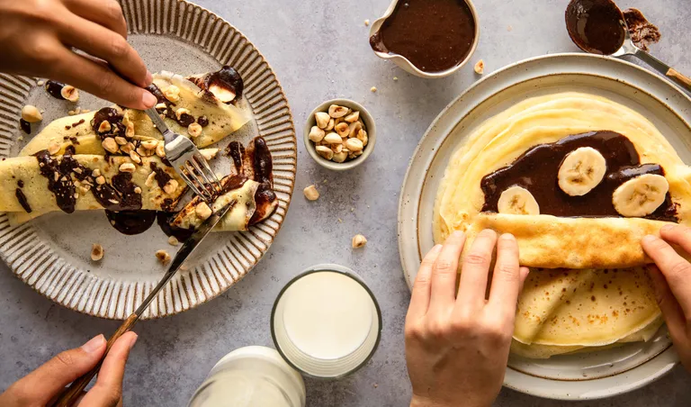 Frische Palatschinken werden mit selbstgemachter Nuss-Nougatcreme, Bananenscheiben und Haselnüssen gefüllt und serviert.