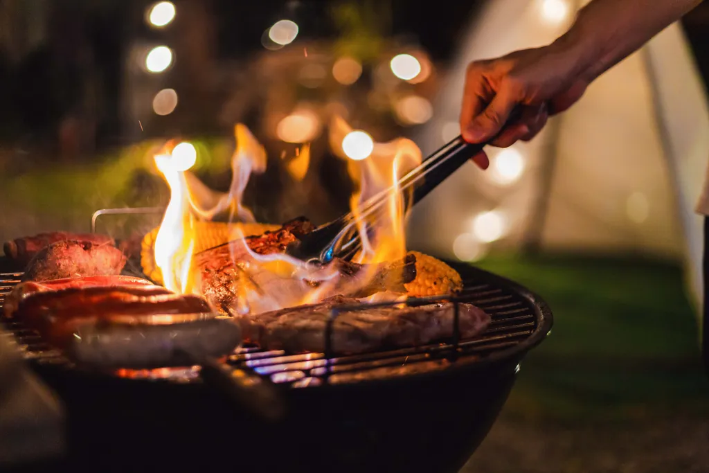 Eine Person beim Grillen auf einem Grill mit großen Flammen in der Abenddämmerung