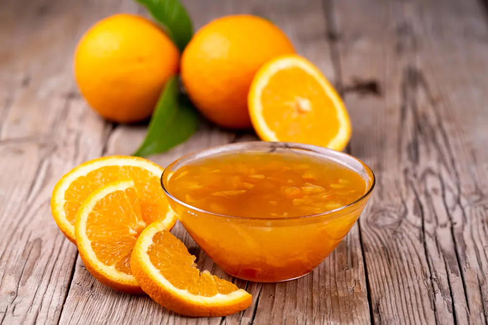 Schüssel mit Orangenmarmelade und frischen Orangen