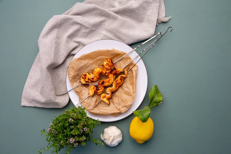 Gegrillte Hühnerspieße auf einem Teller mit Zitrone, Knoblauch und frischen Kräutern