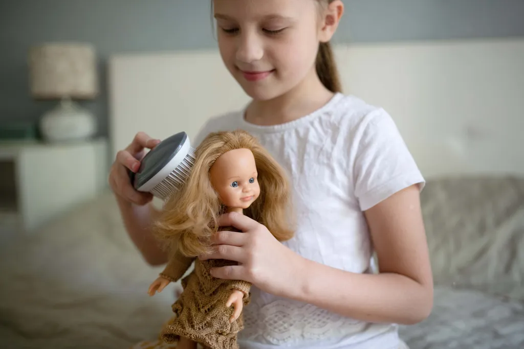 Mädchen kämmt sorgfältig die langen Haare einer Spielpuppe im Kinderzimmer