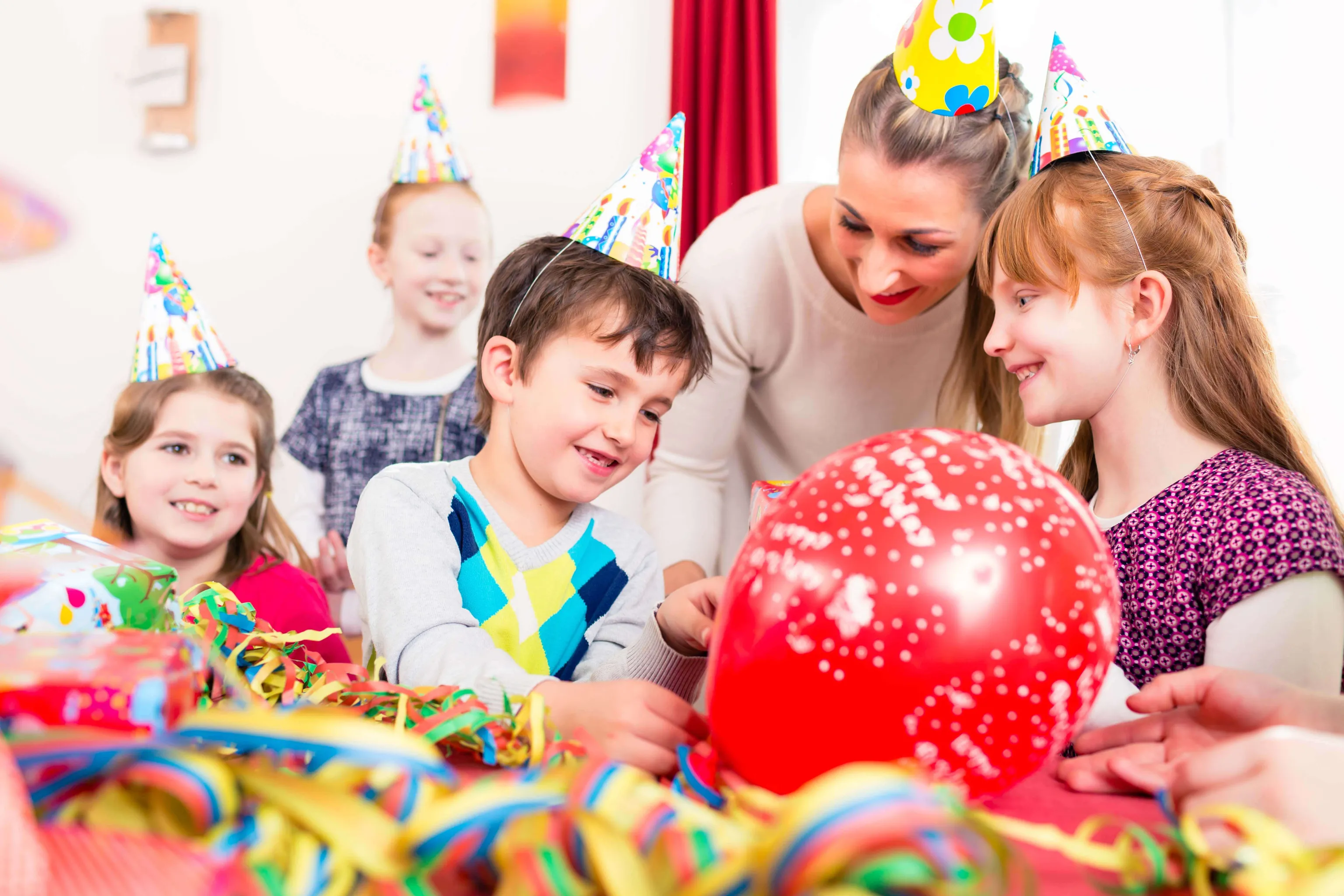 Kinder und Erwachsene feiern gemeinsam einen Kindergeburtstag mit Luftballons und Partyhüten