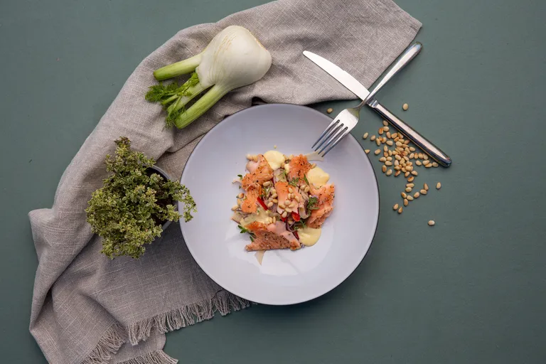 Lachsforellensalat mit Fenchel, Pinienkernen und Aioli auf einem Teller