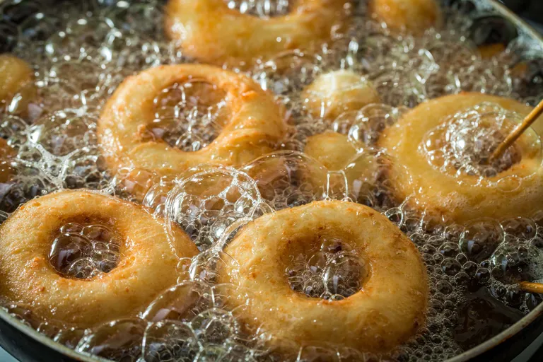 Goldene Krapfen, die in heißem Öl frittieren, umgeben von sprudelndem Schaum.