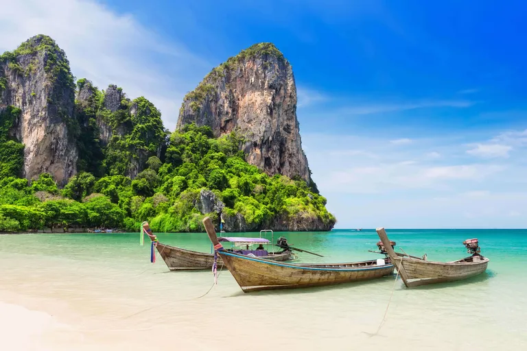 Traditionelle Longtail-Boote an einem tropischen Strand mit Kalksteinfelsen in Thailand