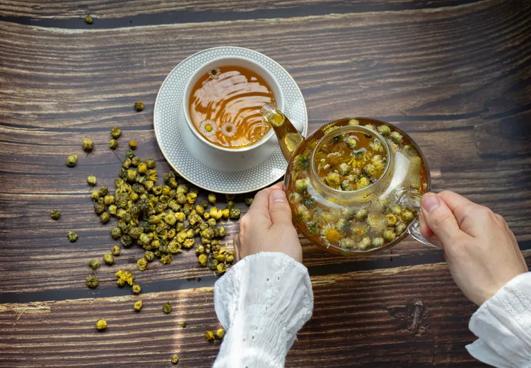Kamillentee wird in einer Glaskanne aufgebrüht und in eine Tasse eingeschenkt