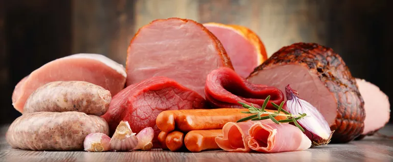 Eine Auswahl an Fleischwaren, darunter Schinken, Würstchen und Wurstwaren, garniert mit einem Rosmarinzweig.