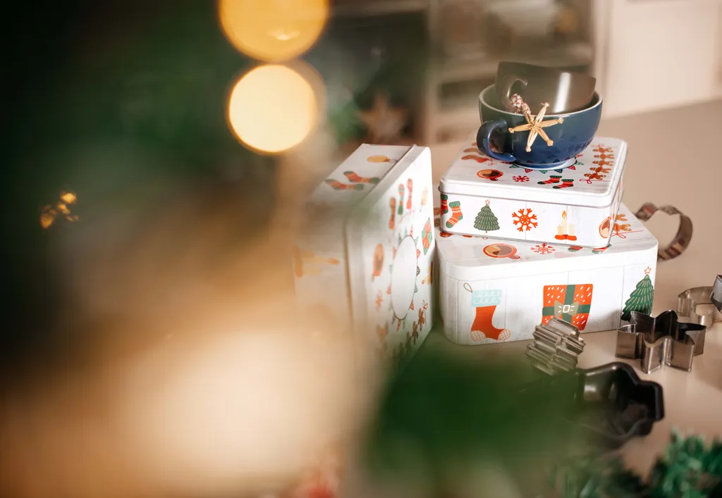 Ein Stapel Keksdosen unter einem Christbaum. Auf dem Stapel stehen zwei Teetassen