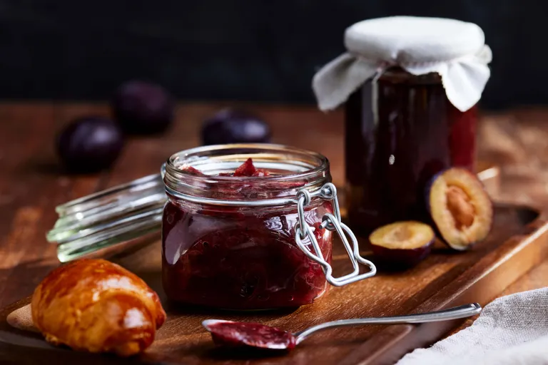 Hausgemachte Powidlmarmelade im Weckglas mit Croissant und frischen Zwetschken auf einem Holztablett