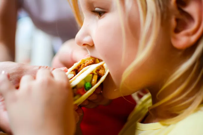 Kind beißt in einen Wrap mit Hackfleisch, Gemüse und Salat