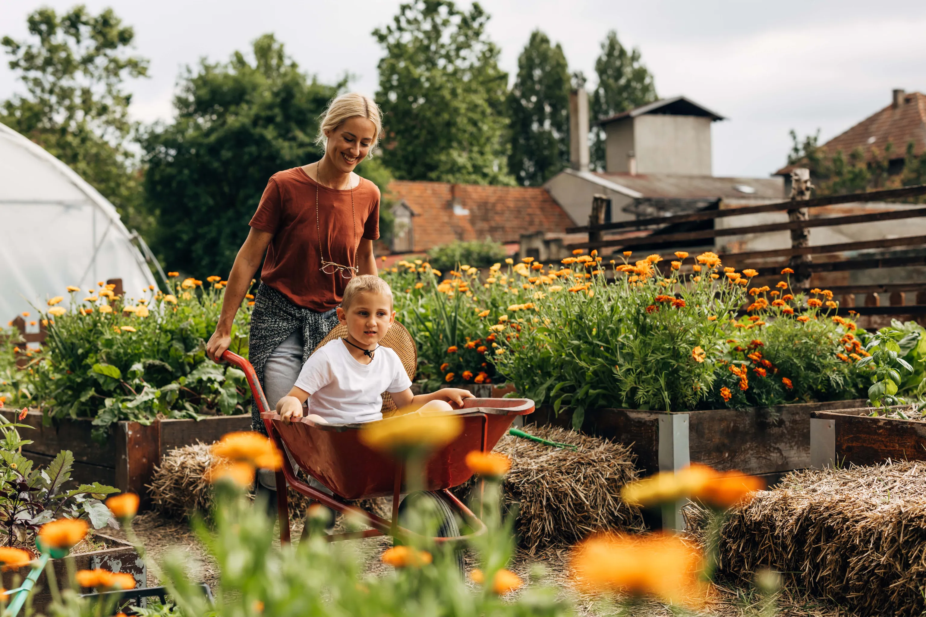 Mutter und Sohn fahren mit einer Schubkarre durch einen Gemüsegarten