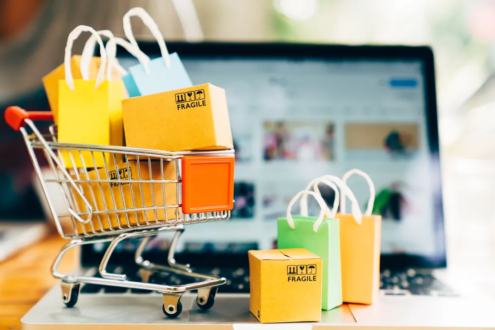 Ein kleiner Einkaufswagen vollbepackt mit kleinen Kartons und Einkaufstaschen, die auf einer Tastatur eines Laptops stehen als Beispiel für Shopping.