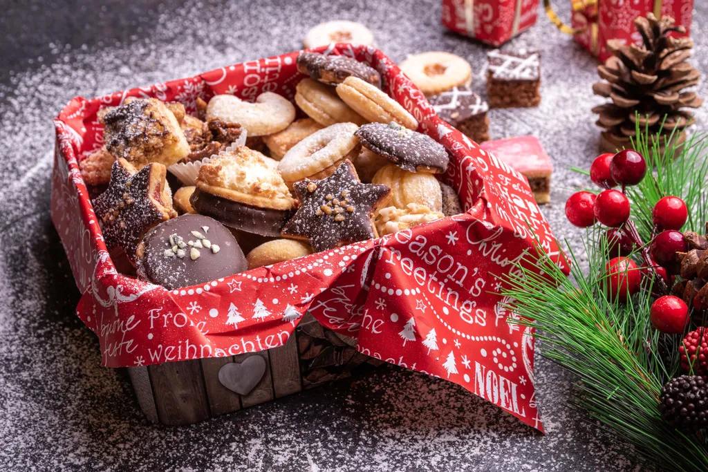 Verschiedene Weihnachtskekse mit Schokolade, Marmelade und Staubzucker liegen in einer weihnachtlich dekorierten Holzkiste.