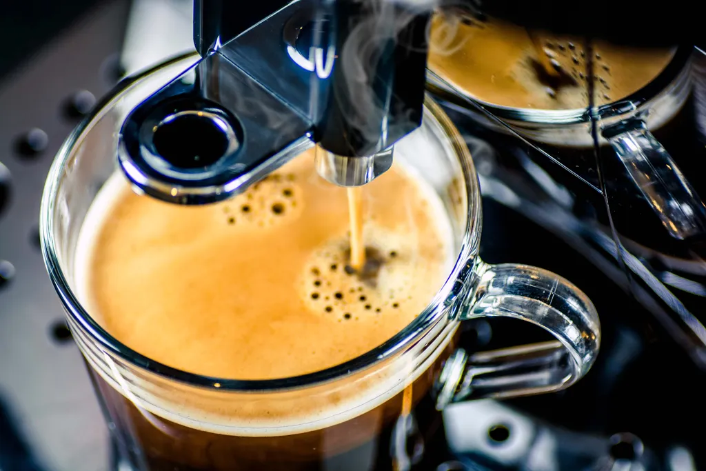 Frisch gebrühter Kaffee mit goldbrauner Crema läuft aus einer Kaffeemaschine in eine Glastasse