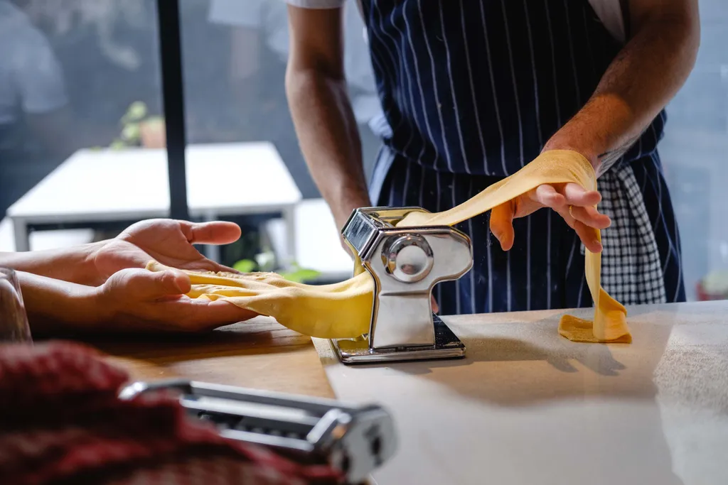 Eine Person macht Pasta selbst, hält Nudeln in den Händen in einer Küche vor einer Pastamaschine