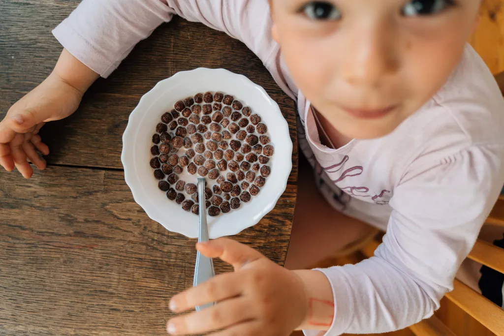 Kind sitzt am Tisch vor einer Schüssel Schokoflakes mit Milch und frühstückt
