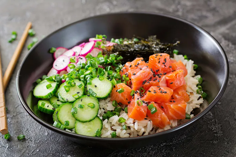 Eine Reis-Bowl, belegt mit Gurke, Radieschen, gewürfeltem Lachs, Seetang und schwarzem Sesam, garniert mit gehackten Frühlingszwiebeln.