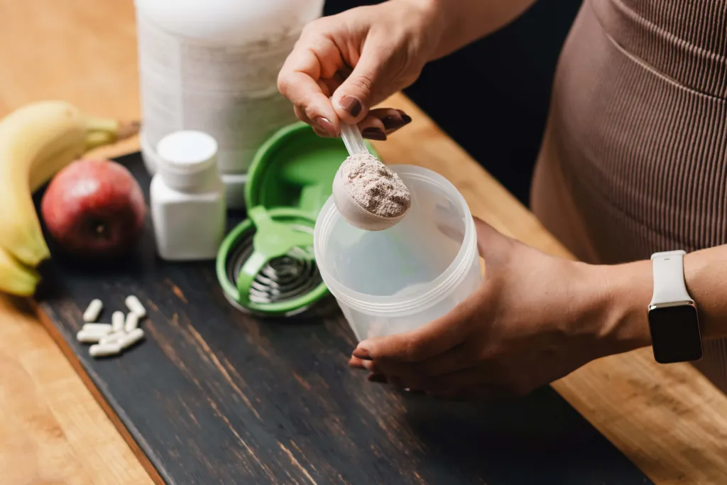 Person füllt Proteinpulver mit Messlöffel in einen Shaker für einen Fitnessshake