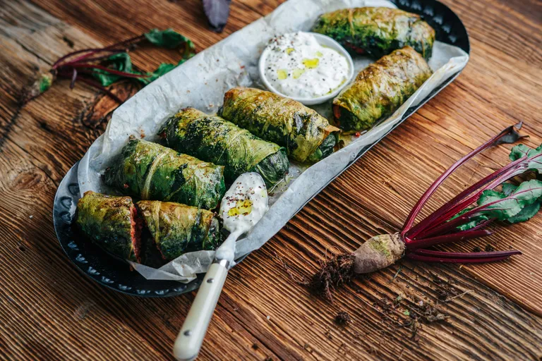 Gebackene Mangoldrouladen mit cremigem Joghurt-Dip auf einem rustikalen Holzbrett