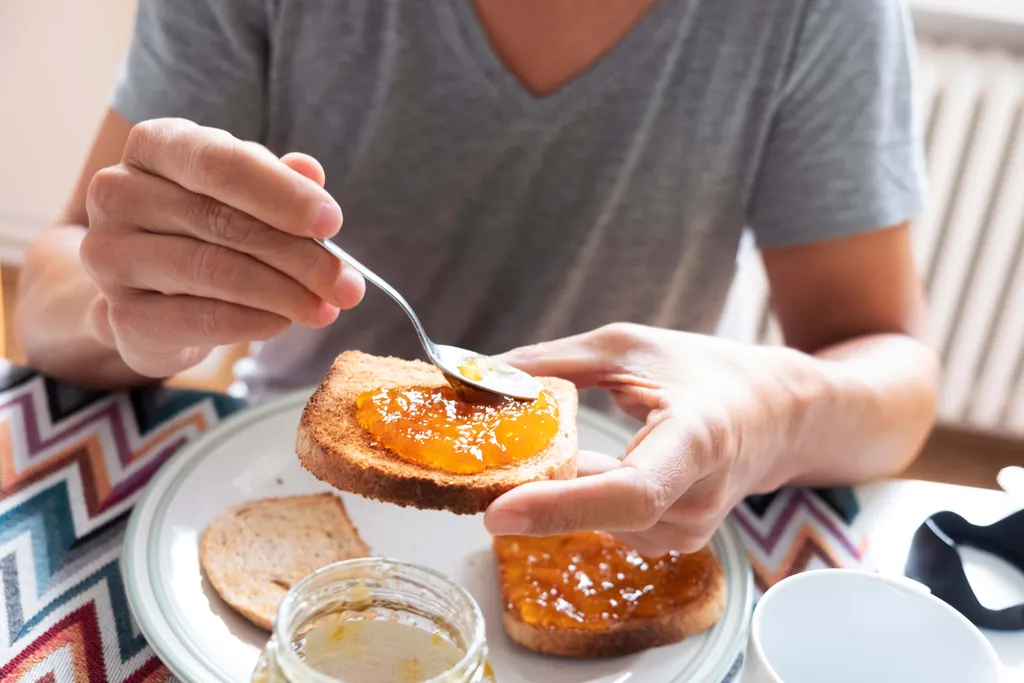 Person streicht Aprikosenmarmelade auf eine Scheibe Toastbrot