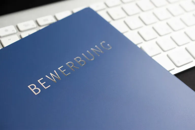 Blaue Bewerbungsmappe mit der Aufschrift Bewerbung liegt vor einer Computertastatur