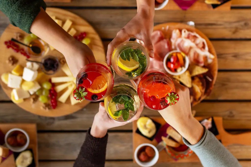 Freunde stoßen mit sommerlichen Cocktails und Aperitif-Getränken an einer reich gedeckten Tafel an