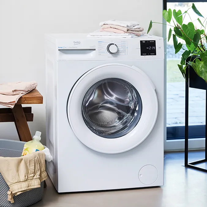 Eine Waschmaschine mit Wäschekorb und gefalteter Wäsche, die oben drauf und nebenan auf einem Hocker liegt.