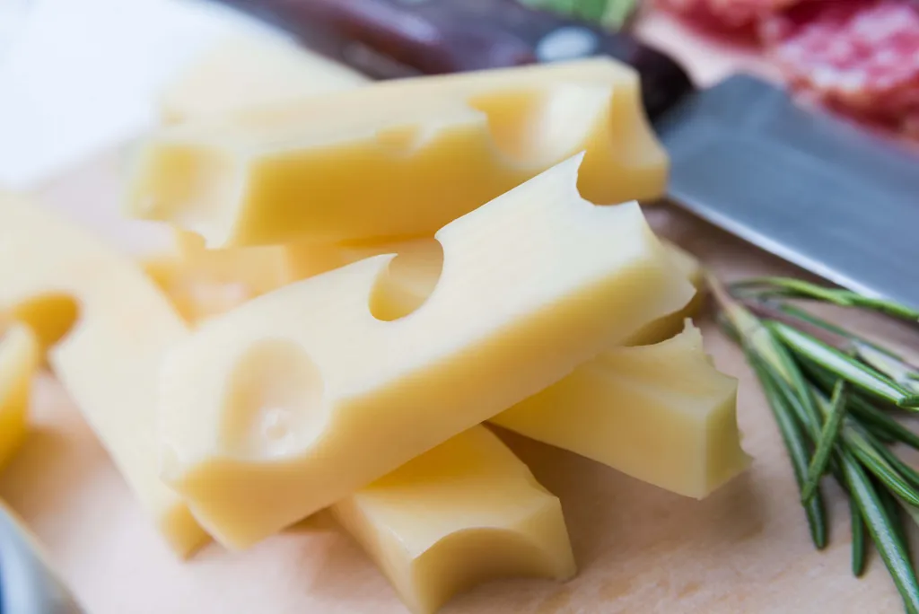 Käse mit Löchern auf einem Holzbrett, dazu ein Messer und Rosmarinzweige.