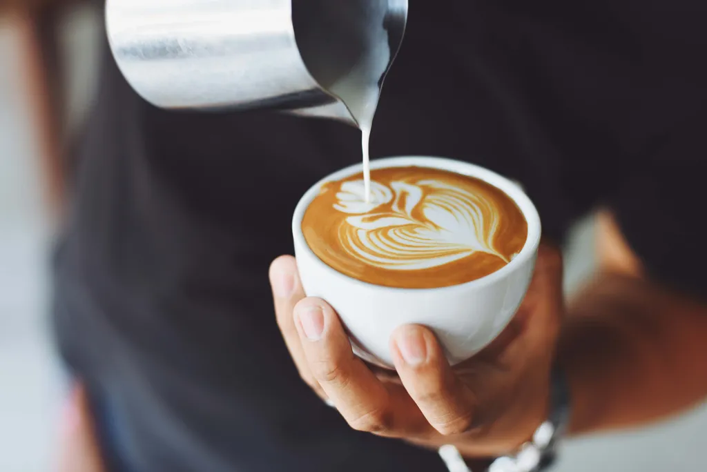Eine Person beim Erstellen eines Latte-Art-Musters mit Milch und Milchschaum in einer Tasse Kaffee
