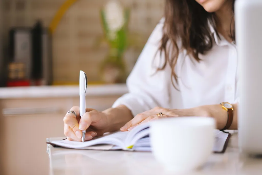 Person schreibt Notizen in ein Notizbuch am Schreibtisch mit einer Tasse Kaffee