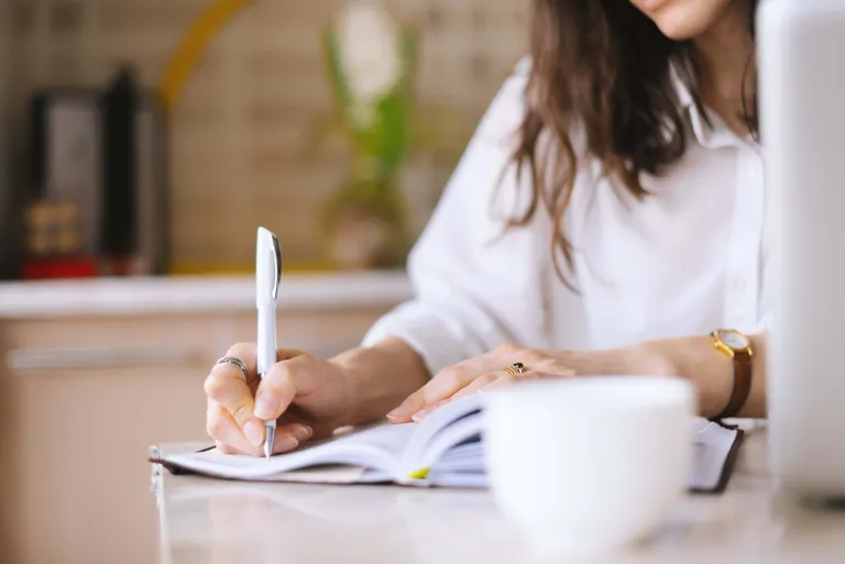 Person schreibt Notizen in ein Notizbuch am Schreibtisch mit einer Tasse Kaffee